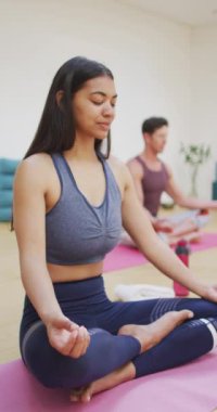Yoga dersinde bacak bacak bacak üstüne atmış, gözleri kapalı meditasyon yapan melez bir kadının dikey videosu. yoga, fitness ve sağlıklı aktif yaşam tarzı.