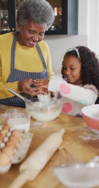 Dikey video mutlu kıdemli Afro-Amerikan büyükanne ve torunu mutfakta yemek pişiriyor. Aile, aile hayatı ve birliktelik kavramı dijital olarak oluşturulmuş video.