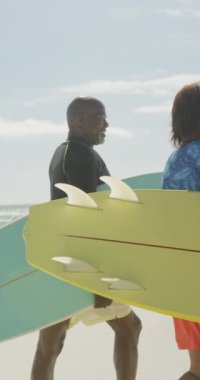 Sunny Beach 'te sörf tahtası olan mutlu Afrikalı Amerikalı çiftin dikey videosu. Plaj tatilinde boş zaman geçirmek.