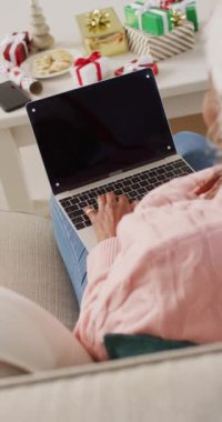 Yaşlı Afro-Amerikan bir kadının Noel 'de dizüstü bilgisayarını kullanırken çekilmiş dikey videosu. Emeklilik, evde vakit geçirme ve Noel konsepti.