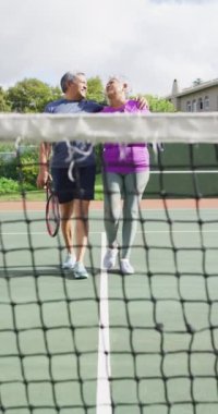 Tenis kortunda kucaklaşan mutlu çift ırklı çiftin dikey videosu. sağlıklı ve aktif emeklilik.