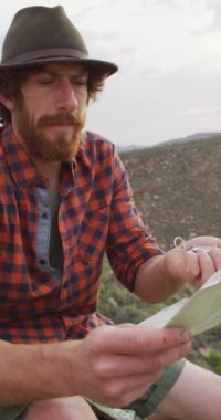 Harita ve pusula ile vahşi doğayı keşfeden beyaz sakallı bir erkeğin dikey videosu. Doğada bedensel kapsama, keşif ve hayatta kalma..