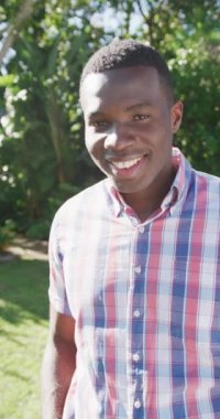 Bahçede kameraya gülümseyen Afro-Amerikan bir adamın dikey video portresi. Mutluluk, sağlık, ev hayatı ve kapsayıcılık kavramı.