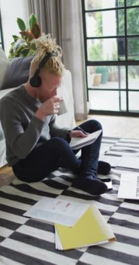 Bir Albino 'nun kahve içerken, kulaklık takarken ve evde grafiklere bakarken dikey görüntüsü. Ev kavramından çalışmak.