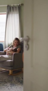 Yeni doğmuş bebeği koltukta emziren mutlu beyaz bir annenin dikey videosu. annelik, ebeveyn sevgisi ve yeni doğan bebek konseptiyle ilgilenmek dijital olarak üretilmiş video.
