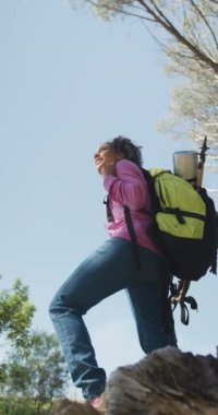 Sırt çantalı mutlu Afro-Amerikan kadının kırsalda yürüyüş yaptığı dikey bir video. Manzaranın tadını çıkarıyor. sağlıklı, aktif açık hava yaşam tarzı ve boş zaman.