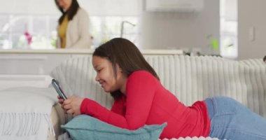 Kanepede akıllı telefonuyla rahatlayan mutlu Asyalı bir kızın videosu. Çocukluk, rahatlama, evde teknoloji konseptiyle zaman geçirme.