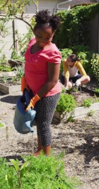 Arka planda kadın ailesi ile bahçede çalışan gülümseyen Afrikalı Amerikalı kızın dikey videosu. Çocukluk yaşam tarzı, bedensel bütünlük, evde iki anneyle vakit geçirmek..