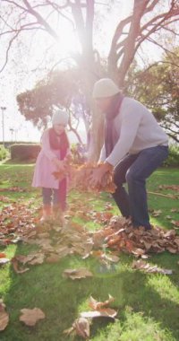 Kafkasyalı mutlu torun ve büyükbabanın yaprakları attığı ve sarıldıkları dikey video. Aile, aile hayatı ve birliktelik kavramı dijital olarak oluşturulmuş video.