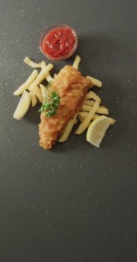 Gri arka planda taze kızarmış balık ve patates cipsinin dikey videosu. Taze ev yapımı fast food..