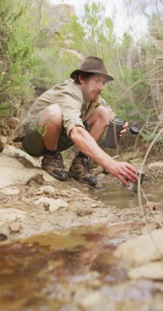 在野外从溪流中收集水的有胡须的高加索男性幸存者的垂直视频 身体的包容性 探索和自然生存 — 图库视频影像