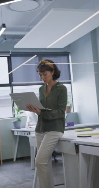 亚洲女商人笑着在办公室使用笔记本电脑的垂直视频 在现代化的办公室工作 — 图库视频影像
