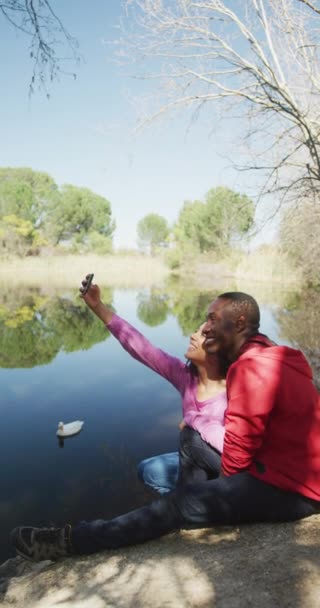 Pionowe Wideo Szczęśliwej Różnorodnej Pary Zakochanej Robiącej Selfie Nad Jeziorem — Wideo stockowe
