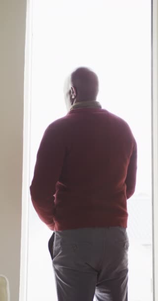 非洲裔美国人站在窗前向外看的垂直视频后视镜 老年生活方式 退休生活方式 积极闲暇时间 — 图库视频影像