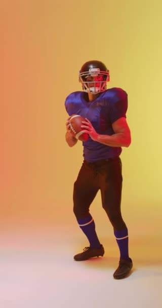 美国白人男性足球运动员持球的垂直视频 带有霓虹灯橙色照明 培训和积极生活方式概念 — 图库视频影像