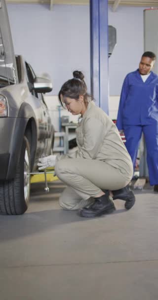 出産の女性の車の整備士の垂直ビデオ変更タイヤ 車の修理店で働くと小さな女性的なビジネスコンセプトを実行している — ストック動画