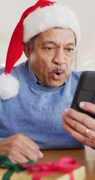 スマートフォンでクリスマスのビデオ通話を作るサンタの帽子の幸せなシニアの助産師の垂直ビデオ クリスマス グローバルなコミュニケーション 包括性とシニアライフスタイルの概念 — ストック動画