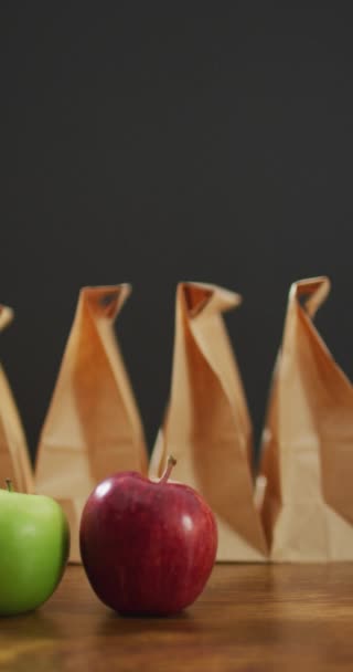 红色和绿色苹果与一排包装好的午餐纸袋和灰色背景的垂直视频 健康饮食 食物和营养 — 图库视频影像
