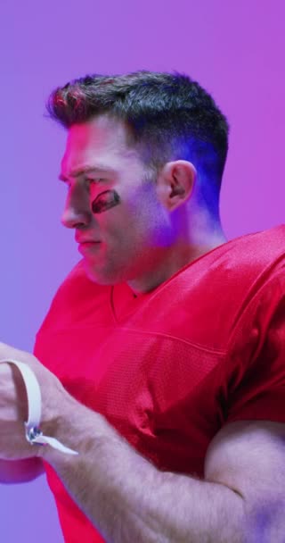 ネオン紫色の照明と ヘルメットを身に着けている白人男性アメリカンフットボール選手の垂直ビデオ スポーツ トレーニング アクティブなライフスタイルの概念 — ストック動画