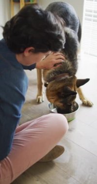 Evinde köpeğini okşayan mutlu beyaz kadının dikey videosu. Evde birlikte vakit geçirmek..