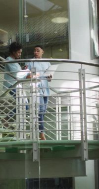 Mutlu kadın ve erkek iş arkadaşlarının merdivenlerde konuştuğu dikey video. İş adamları ve ofis kavramında çalışmak.