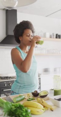 Afro-Amerikan bir kadının mutfakta sağlıklı bir şeyler içtiği dikey bir video. Evde yalnız zaman geçirmek..