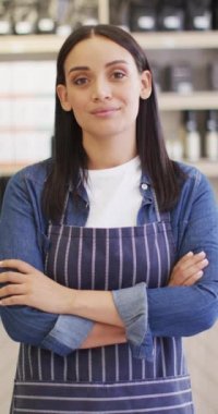 Kafede kolları çaprazlanmış gülümseyen melez kadın baristanın dikey videosu. bağımsız kafe işi.