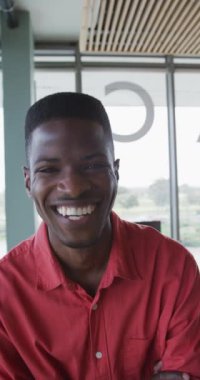 Modern ofisteki gülümseyen Afrikalı Amerikalı adamın kameraya gülüşünün dikey videosu. Yaratıcı bir iş yerindeki bedensel kapsayıcılık.