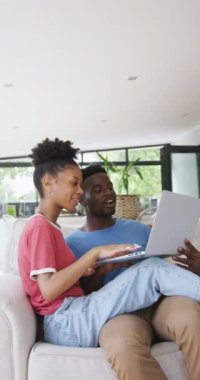 Evde dizüstü bilgisayar kullanan mutlu Afro-Amerikan çiftin dikey videosu. Evde birlikte vakit geçirmek..