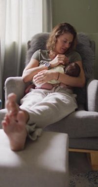 Yeni doğmuş bebeği koltukta emziren mutlu beyaz bir annenin dikey videosu. annelik, ebeveyn sevgisi ve yeni doğan bebek konseptiyle ilgilenmek dijital olarak üretilmiş video.