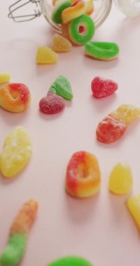 Cam kavanozdan pembe arka plana dökülen jöle şekerlerinin dikey videosu. tatlı yiyecekler ve şeker.