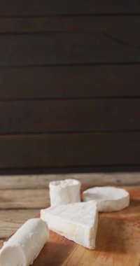 Tahta kesim tahtası ve kırsal arka planda birkaç çeşit taze peynirin dikey videosu. Peynir, süt ürünleri ve taze ürünler.