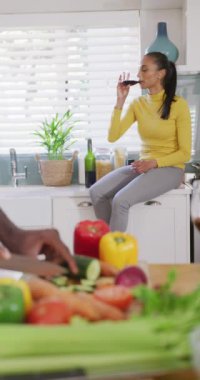 Partnerin yemek hazırlarken, melez kadının mutfakta şarap içtiği dikey video. Mutluluk, sağlık, ev hayatı ve kapsayıcılık kavramı.