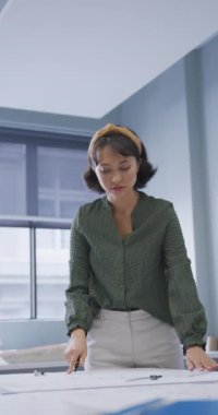 Asyalı iş kadınının ofiste şemalarla çalıştığı dikey bir video. Modern bir ofiste çalışıyorum..