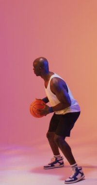 Pembe arka planda topu atan Afro-Amerikan erkek basketbolcunun dikey videosu. Spor ve rekabet konsepti.