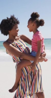 Sahilde kızı olan mutlu bir Afrikalı Amerikalı annenin dikey videosu. Aile birlikte vakit geçiriyor..