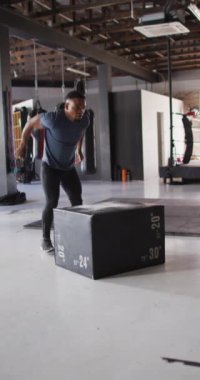 Formda bir Afrikalı Amerikalının spor salonunda bloğa atladığı dikey bir video. aktif, formda, sportif ve sağlıklı yaşam tarzı, spor konsepti egzersizi.