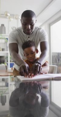 Görme engelli oğluna kör alfabesiyle yardım eden mutlu Afro-Amerikan babasının dikey videosu. Aile, kapsayıcılık ve zorlukların üstesinden gelme kavramı.