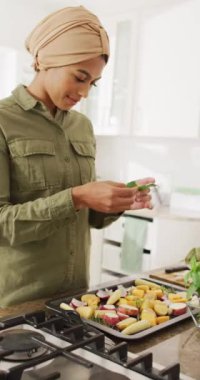 Mutfakta yemek hazırlayan tesettürlü melez kadının dikey videosu. Yaşam tarzı, yemek pişirme, evde boş zaman geçirme..