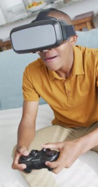 Video oyunları oynayan, VR kulaklıklı mutlu Afrikalı Amerikalı çocuğun dikey videosu. Rahatlayın, rahatlayın, evde teknolojiyle vakit geçirin..