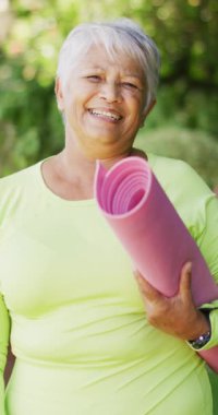 Bahçesinde yoga minderi olan mutlu son sınıf melez kadın portresinin dikey videosu. sağlıklı, aktif emeklilik.