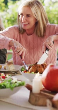 Açık hava yemek masasında tavuk kesen yaşlı beyaz kadının dikey videosu. Dijital olarak üretilen ev hayatı, sağlık ve mutluluk konsepti.
