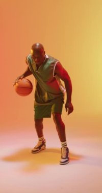 Turuncu arka planda zıplayan Afrikalı Amerikalı erkek basketbolcunun dikey videosu. Spor ve rekabet konsepti.
