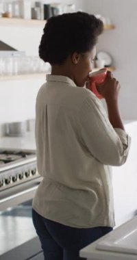 Evde kahve içen mutlu Afro-Amerikan kadının dikey videosu. Evde yalnız zaman geçirmek..