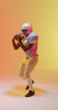 Neon turuncu ışıklandırmalı Afro-Amerikan erkek Amerikan futbolcusunun dikey videosu. Spor, hareket, eğitim ve aktif yaşam tarzı kavramı.