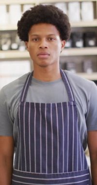 Kafede önlük giymiş, gülümseyen Afrikalı Amerikalı bir baristanın dikey videosu. bağımsız kafe işi.