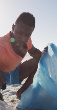 Afrika kökenli Amerikalı bir adamın sahildeki atıkları ayırdığı dikey bir video. Plaj tatilinde boş zaman geçirmek.