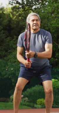 Bahçede tenis oynayan yaşlı, çift ırklı adamın dikey videosu. sağlıklı ve aktif emeklilik.
