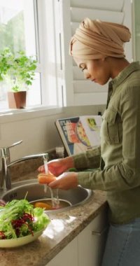 Türbanlı bir kadının mutfakta sebze yıkarken çekilmiş dikey videosu. Yaşam tarzı, yemek pişirme, evde boş zaman geçirme..
