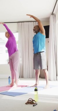 Evde yoga yapan mutlu yaşlı çiftin dikey videosu. Mutluluk, sağlık, emeklilik, birliktelik, ev hayatı ve kapsayıcılık kavramı.